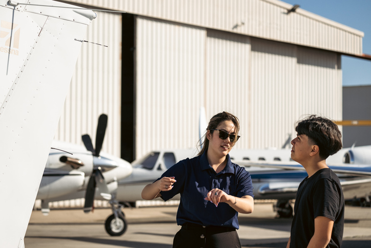 Professional aviation instructor giving advice to a student in front of a plane and hangar